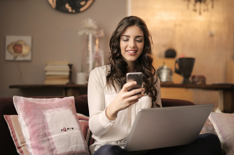 mulher com celular na mao em frente o notebook