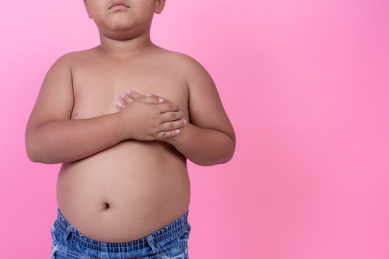 Menino obeso que está acima do peso em um fundo rosa.
