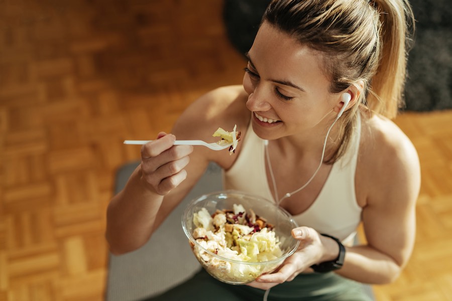 mulher feliz comendo salada após o treino.