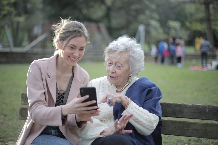 Mulher mais jovem mostrando o celular para uma mulher idosa