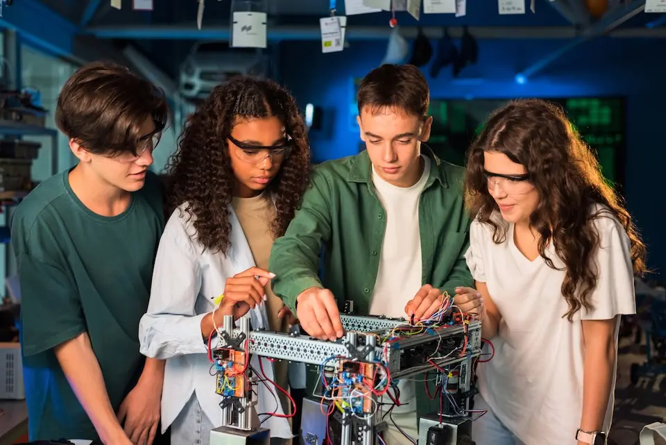 Grupo de jovens fazendo experimentos de robótica em um laboratório. Meninas com óculos de proteção