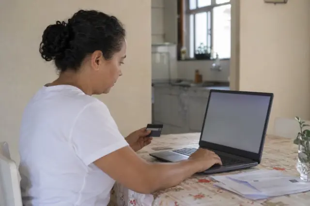Pessoa usa cartão de crédito e notebook para regularizar conta de água