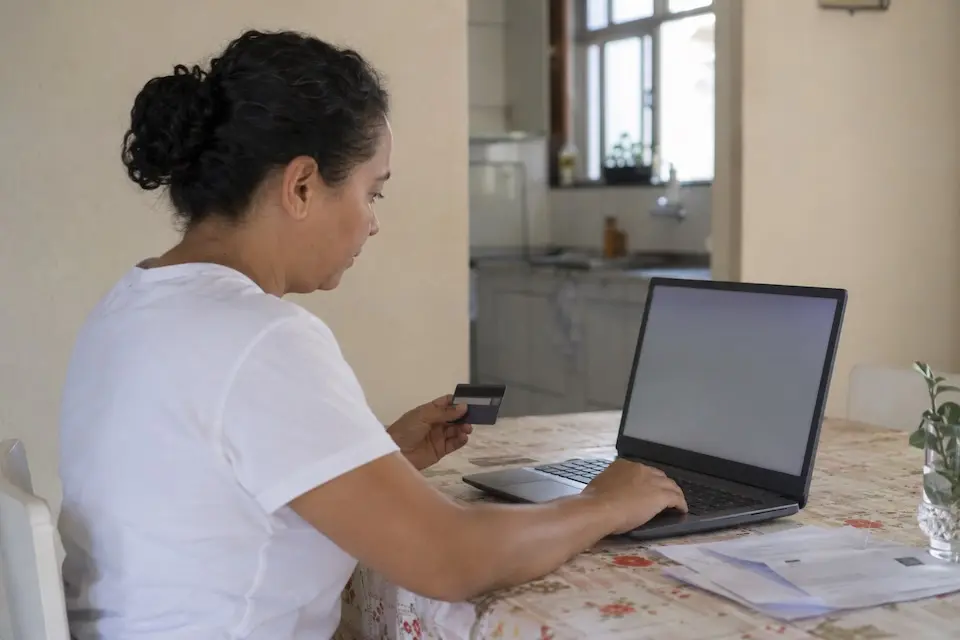 Pessoa usa cartão de crédito e notebook para regularizar conta de água
