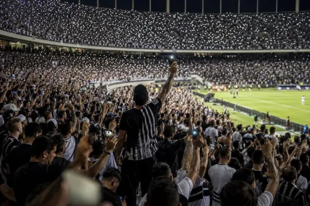 Torcida do Corinthians em estádio com celulares acesos durante manifestação de apoio a jogador