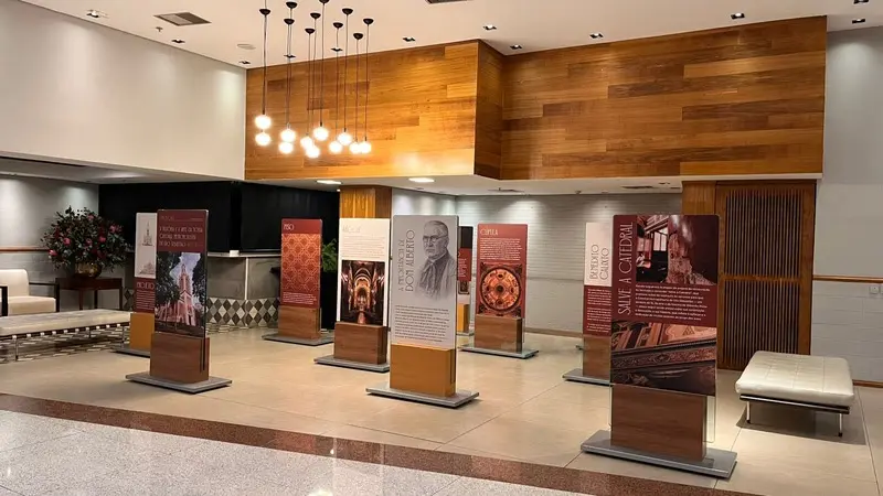 painéis expositivos verticais com textos e imagens dispostos em corredor de shopping, bancos e luminárias no teto