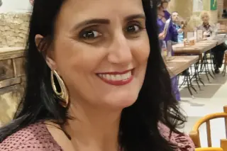 Mulher sorrindo em retrato em ambiente interno com mesas e livros ao fundo