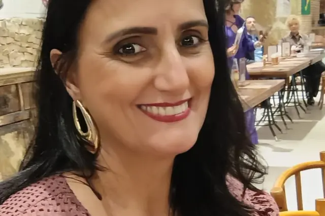Mulher sorrindo em retrato em ambiente interno com mesas e livros ao fundo