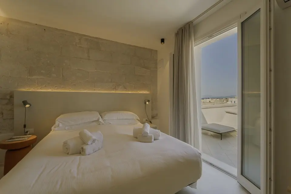 Quarto com cama de casal, parede de pedra e porta de vidro que dá para terraço com espreguiçadeira
