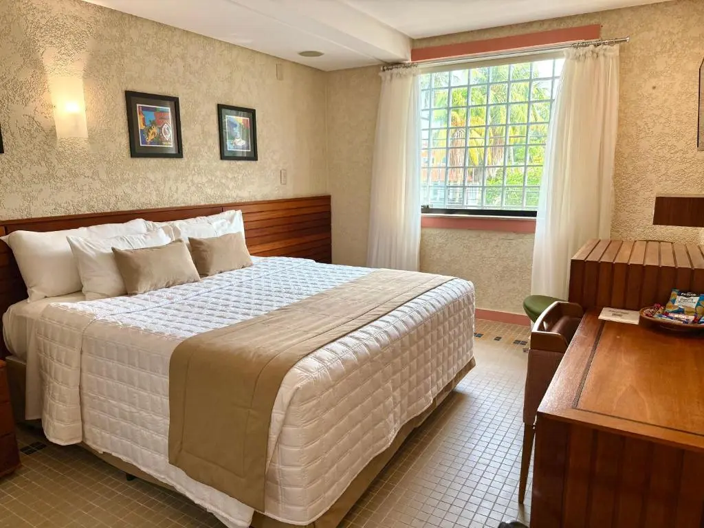 Quarto com cama, cabeceira de madeira e janela com grades