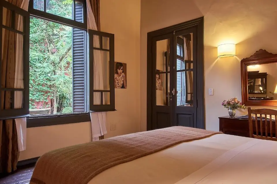 Quarto com cama, janelas abertas e mesa com vaso de flores