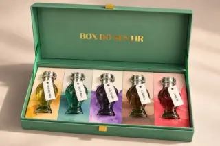 caixa verde aberta com cinco frascos de vidro coloridos alinhados sobre painéis e texto dourado "BOX DO SENTIR" na tampa interna