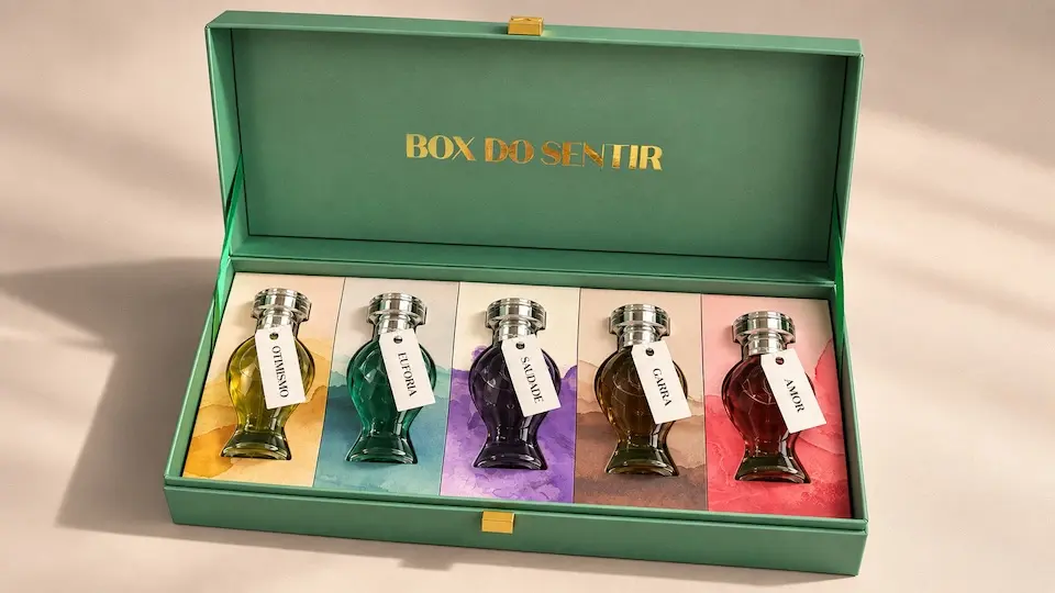 caixa verde aberta com cinco frascos de vidro coloridos alinhados sobre painéis e texto dourado "BOX DO SENTIR" na tampa interna