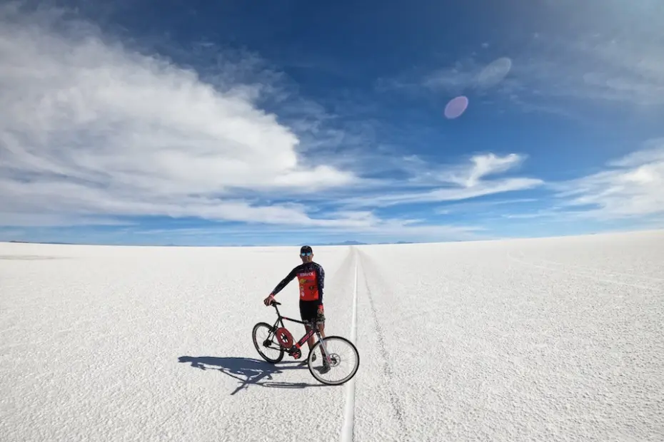 Ciclista parado ao lado de bicicleta sobre o Salar de Uyuni com céu azul e nuvens