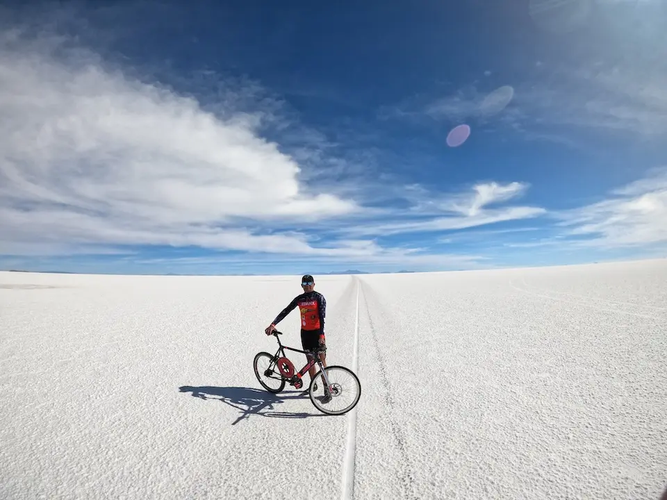 Ciclista parado ao lado de bicicleta sobre o Salar de Uyuni com céu azul e nuvens
