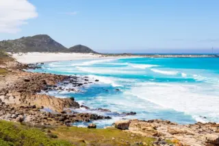 Costa rochosa com praia de areia clara e mar azul-turquesa sob céu claro
