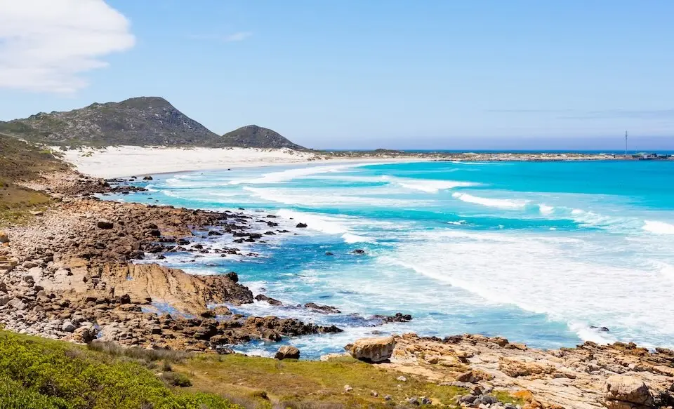 Costa rochosa com praia de areia clara e mar azul-turquesa sob céu claro