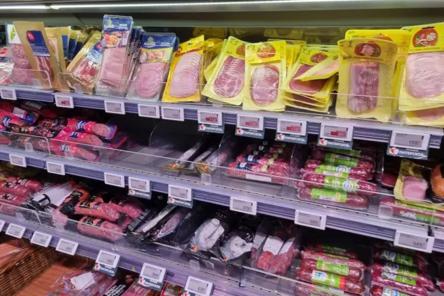 prateleira refrigerada com embalagens de embutidos e produtos cárneos processados fatiados e em pacotes, com etiquetas de preço visíveis