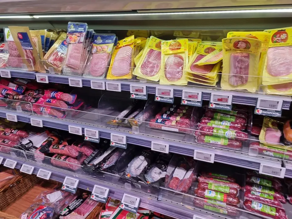 prateleira refrigerada com embalagens de embutidos e produtos cárneos processados fatiados e em pacotes, com etiquetas de preço visíveis