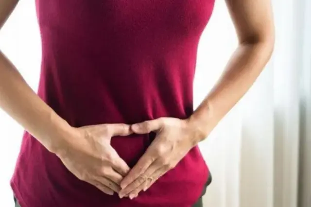 Pessoa com camiseta vermelha segurando a região inferior do abdômen com as mãos
