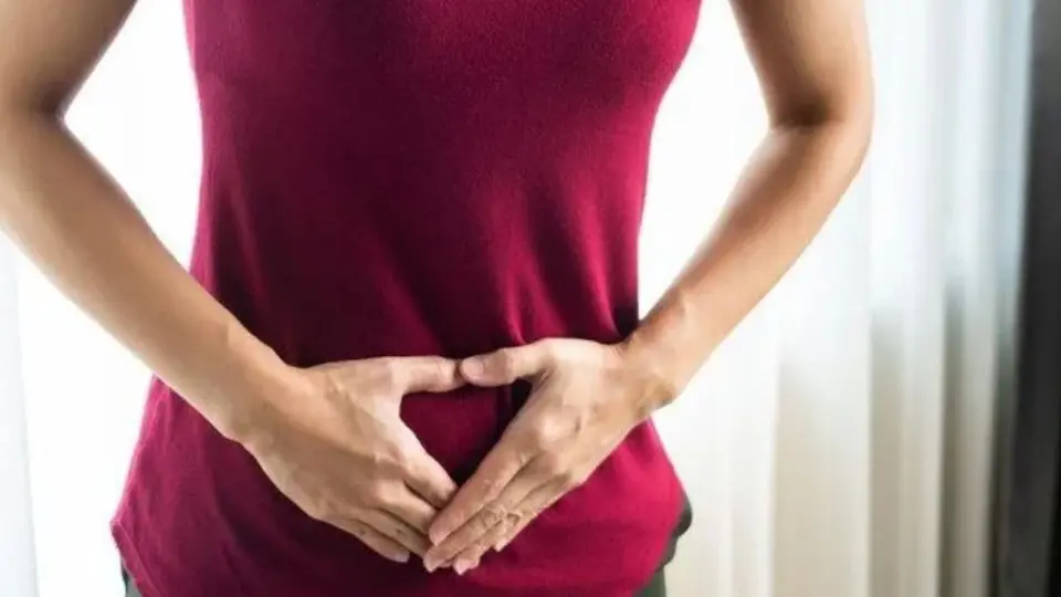Pessoa com camiseta vermelha segurando a região inferior do abdômen com as mãos