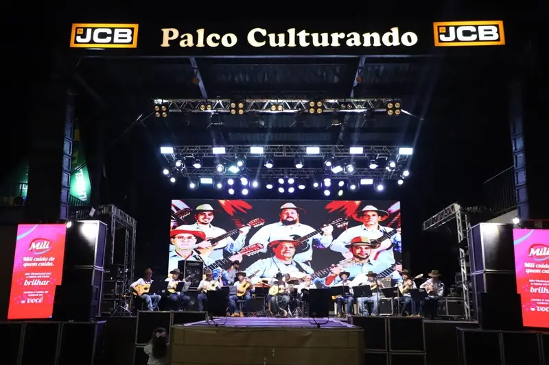 Palco Culturando iluminado com um grupo de músicos tocando violões e outros instrumentos, com telão ao fundo mostrando imagens dos artistas