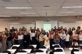 Grupo de pessoas posando em sala de aula com tela de projeção e carteiras no primeiro plano