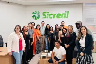 Grupo de pessoas posando em sala com logotipo verde do Sicredi na parede ao fundo