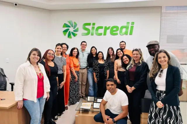 Grupo de pessoas posando em sala com logotipo verde do Sicredi na parede ao fundo