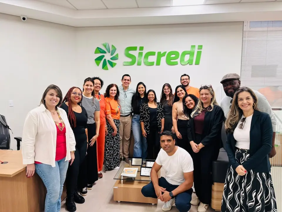 Grupo de pessoas posando em sala com logotipo verde do Sicredi na parede ao fundo