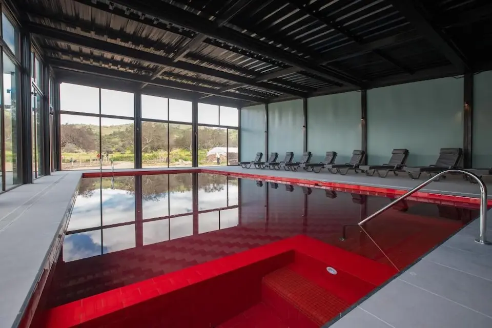 Piscina interna com azulejos vermelhos e espreguiçadeiras junto a janelas panorâmicas