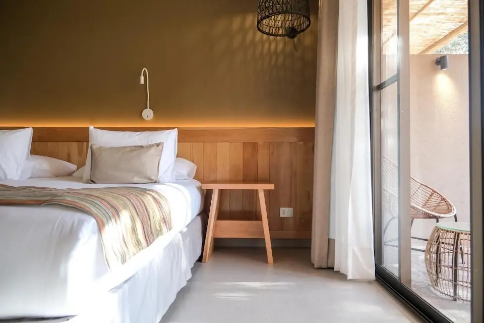Quarto com cama e decoração em tons terrosos e porta de vidro para varanda