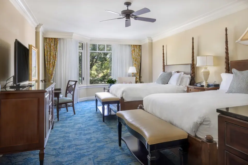 Quarto de hotel com duas camas, móveis de madeira escura e carpete azul