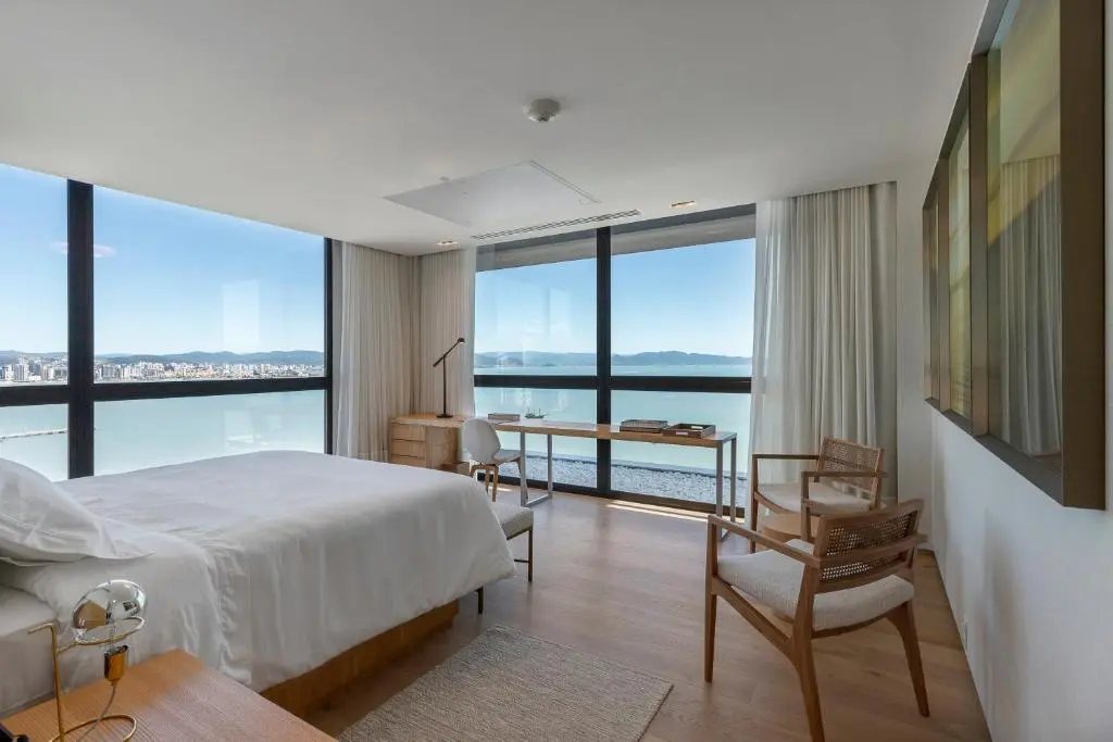 quarto de hotel com cama de casal e janelas amplas mostrando vista do mar e escrivaninha junto à janela