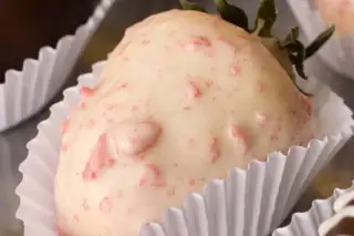 Morango coberto por chocolate branco com pequenos cristais avermelhados, em forminha de papel branca