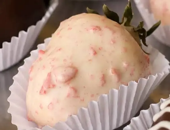 Morango coberto por chocolate branco com pequenos cristais avermelhados, em forminha de papel branca