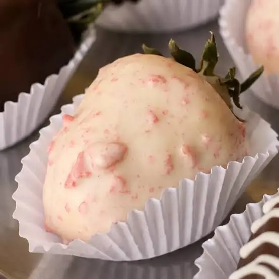 Morango coberto por chocolate branco com pequenos cristais avermelhados, em forminha de papel branca