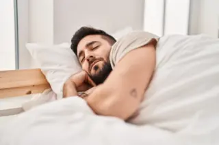 homem deitado na cama dormindo de lado com roupa de cama branca e travesseiro