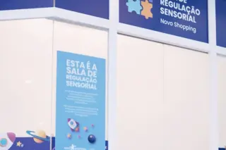 Fachada da Sala de Regulação Sensorial com letreiro azul 'Sala de Regulação Sensorial Novo Shopping' e adesivos com elementos espaciais nas portas de vidro