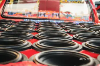 Vários subwoofers circulares pretos montados em painel vermelho de veículo, alinhados em fileiras