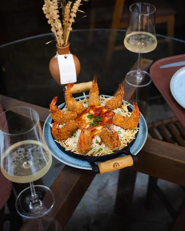 prato redondo com arroz e camarões empanados dispostos em volta, sobre mesa de vidro com duas taças de vinho