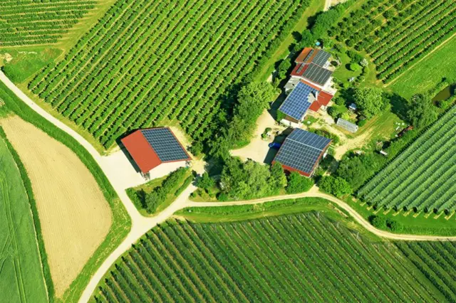 Vista aérea de propriedade rural com vários telhados com painéis solares, cercada por lavouras e estradas de terra