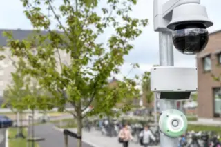Câmera dome e módulos de sensores montados em um poste com fundo desfocado de campus, árvores, bicicletas e pessoas caminhando