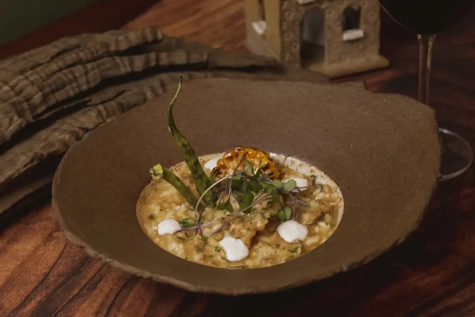 risoto cremoso servido em tigela rústica, guarnecido com milho grelhado em rodela, microverdes e pequenas gotas de creme