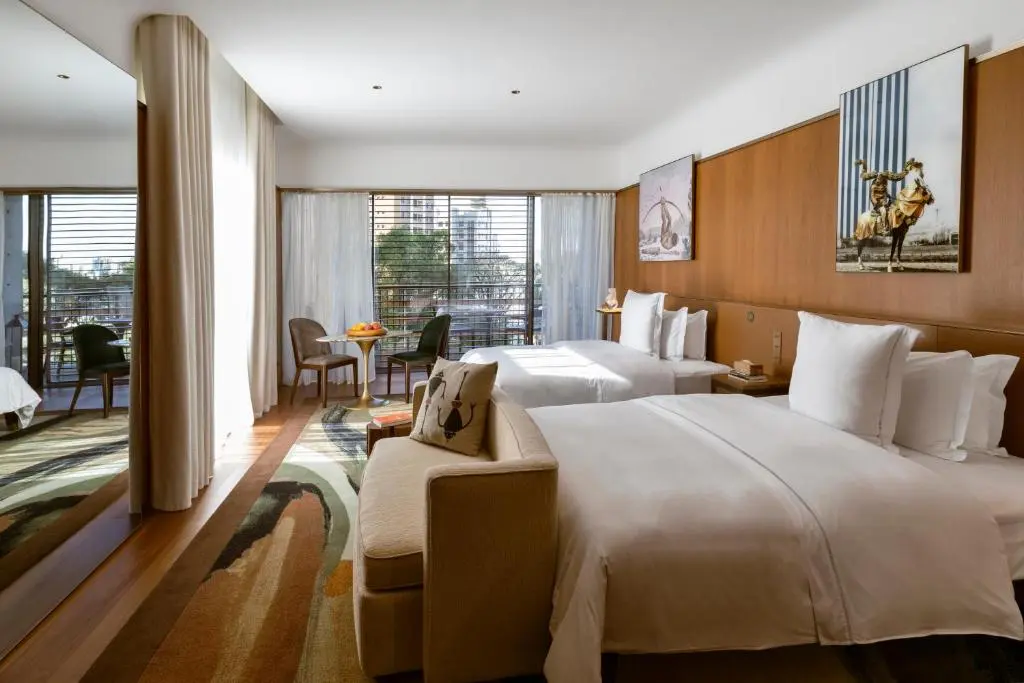Quarto com duas camas de casal, sofá no pé da cama e janelas amplas