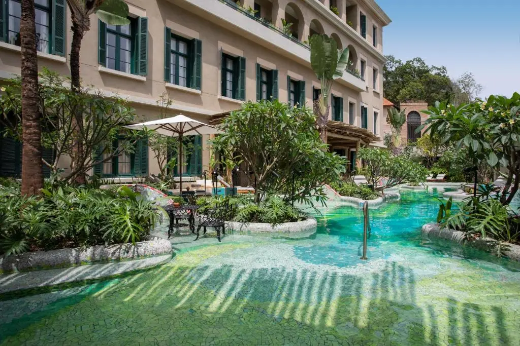 Piscina ao ar livre cercada por vegetação e fachada do hotel