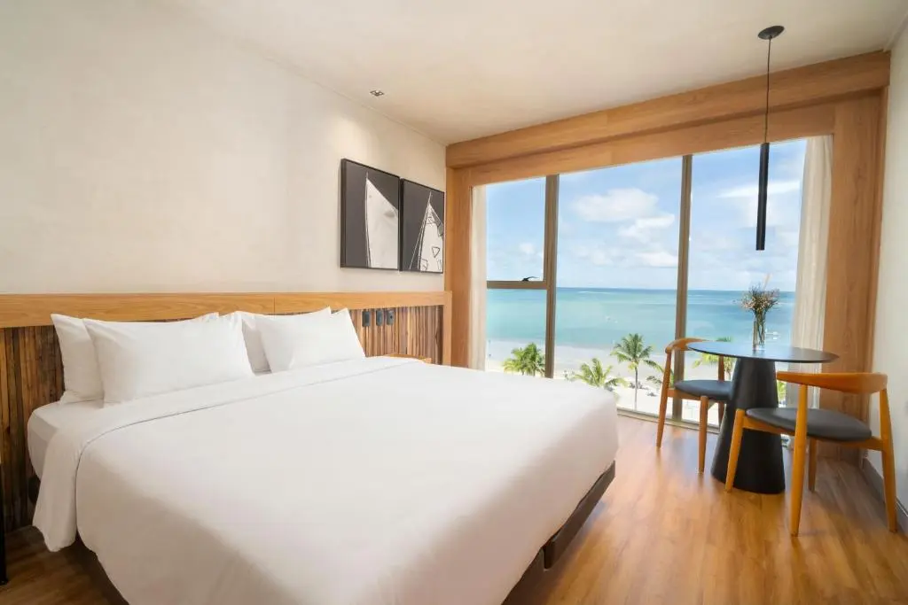 quarto de hotel com cama grande e janela panorâmica mostrando praia e mar ao fundo