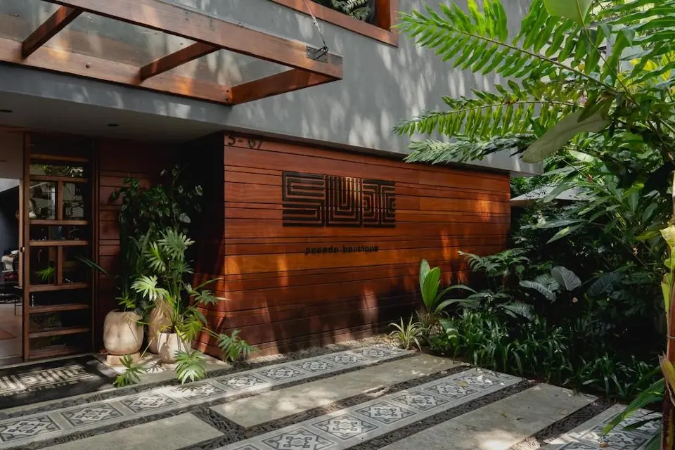 Entrada com fachada de madeira e jardim com plantas tropicais
