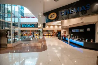 Lobby do cinema UCI no RibeirãoShopping com letreiro 'UCI Cinemas', sinal 'IMAX', balcões de atendimento e algumas pessoas