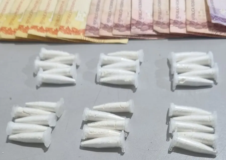 Microtubos plásticos brancos dispostos em grupos sobre superfície cinza e cédulas de dinheiro parcialmente visíveis no topo