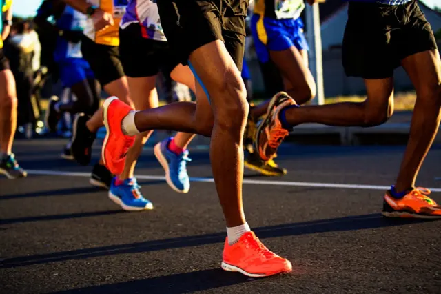 pés de corredores em corrida, close em tênis coloridos no asfalto